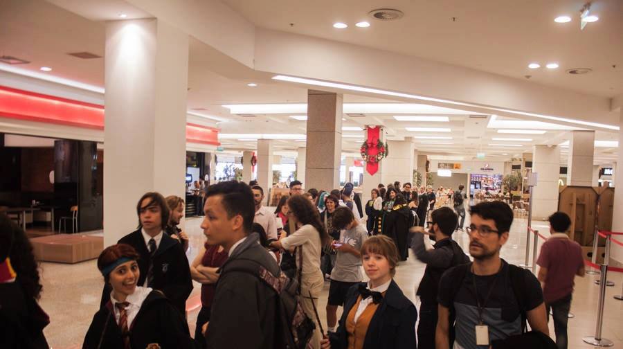 Fotografia retangular horizontal   da pré-estreia do filme Animais fantásticos e onde habitam. Ano: 2017. No corredor iluminado de um shopping, forma-se uma extensa fila. Em primeiro plano, as pessoas na fila estão caracterizadas com vestimentas que fazem referência ao filme “Animais fantásticos e onde habitam”. Fim da descrição