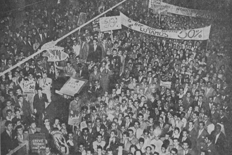 Fotografia em preto e branco, uma multidão nas ruas do centro de Porto Alegre, 1947,  algumas pessoas segurando cartazes. [Fim da descrição]