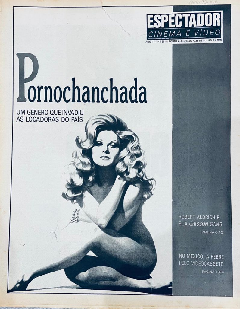 Imagem  em preto e branco  vertical da capa  da Revista Espectador, Cinema e Vídeo, de julho de 1988.  A capa é composta por desenho e textos. Na parte superior nome da revista Espectador, Cinema e Vídeo. Abaixo a palavra Pornochanchada e o desenho de uma mulher nua de cabelos compridos e ondulados, sentada, de braços cruzados em frente ao peito. [Fim da descrição]